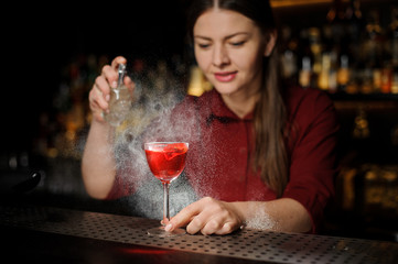 Female bartender decorating a glass of alcoholic cocktail with sparay