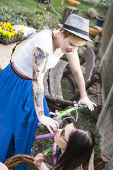 Two young girl friends in back yard talking and enjoying the day. One of them wearing a hat and sitting on colorful bike