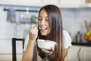 Attractive woman eating bowl of cereal and fruit at home in kitchen