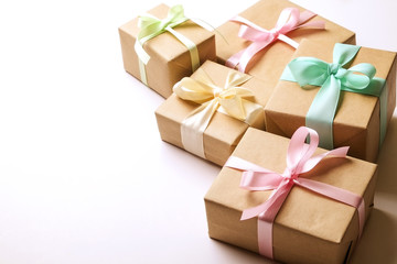 Simple composition with multiple presents wrapped in hand made blank craft paper gift wrap, pastel satin bow. Simple giftbox, wrapping, giftwrap, silk ribbon. White background, close up, copy space.