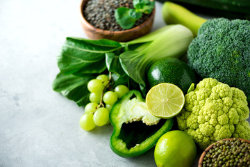 Organic green vegetables and fruits on grey background. Copy space, flat lay, top view. Green apple, zucchini, cucumber, avocado, kale, lime, kiwi, grapes, banana, broccoli, marbled lentils, mung bean