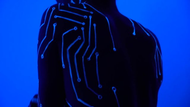 A girl with a bodypainting on her body in the form of a microcircuit dances at an exhibition in the ultraviolet light