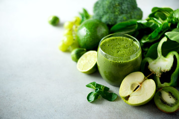 Glass with green health smoothie, kale leaves, lime, apple, kiwi, grapes, banana, avocado, lettuce. Copy space. Raw, vegan, vegetarian, alkaline food concept.