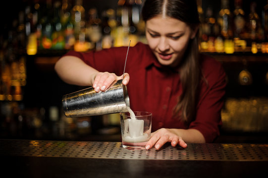 Female bartender pouring out a cocktail from the shaker