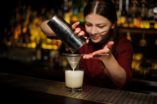 Female bartender pouring out a cocktail from the shaker through the bolter