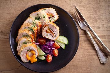 Chicken wrapped with ham and cheddar cheese; vegetables in black plate on wooden table. horizontal