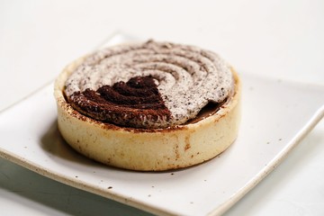 Delicious dessert, Italian dessert, rounded tiramisu tart placed on white plate and placed on white table. Tiramisu cake with Cinnamon and Coffee