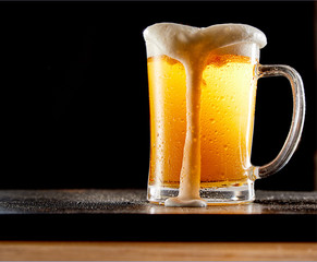 Mug of beer with thick foam on black background