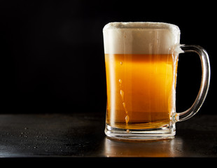 Mug of beer with thick foam on black background