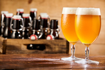 Two chalices of pale beer against box with bottles