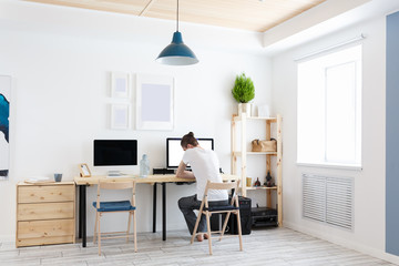 People, business and freelance concept. White modern creative studio interior. Rear view young designer working at desk. Remote work at home