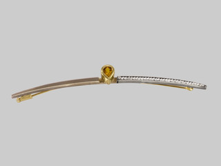 Fototapeta premium Brosche Die Form der Brosche verläuft im leichten Bogen. Die Brosche ist in einer Kombination von Weissgold und Gelbgold gefertigt und poliert. Mittig befindet sich eine Zargenfassung mit einem eingef