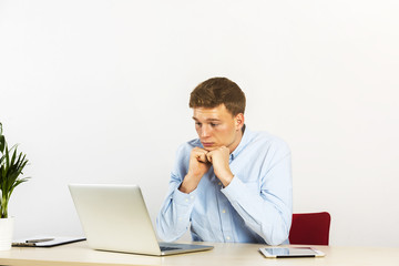 Happy young businessman using laptop at his office desk and thinking, look straight ahead.