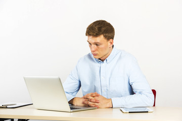 Happy young businessman using laptop at his office desk and thinking, look straight ahead.