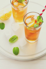Glasses of iced tea with lemon slices and mint on white wooden background. Toned
