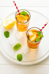 Glasses of iced tea with lemon slices and mint on white wooden background