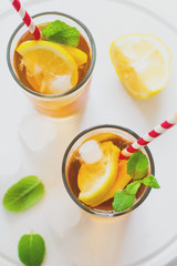 Glasses of iced tea with lemon slices and mint on white wooden background. Toned