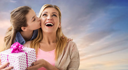 people, holidays and family concept - daughter kissing happy mother and giving her birthday present over evening sky background