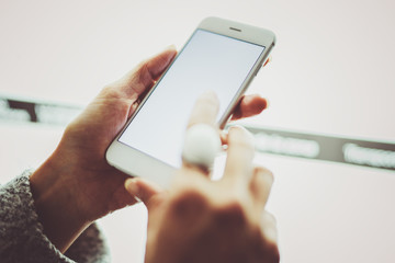 Girl pointing finger on screen smartphone.Female hands texting message mobile phone.Closeup on blurred light coloured background.