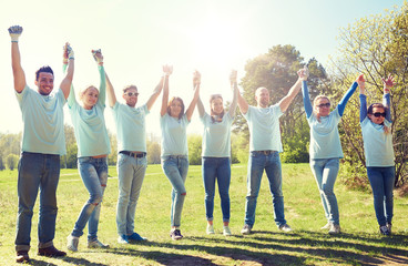 volunteering, charity and people concept - group of happy volunteers holding hands outdoors