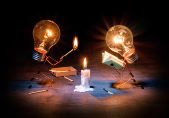 Art composition on the topic of teaching, development or education. Two light bulbs in the form of people near a burning candle