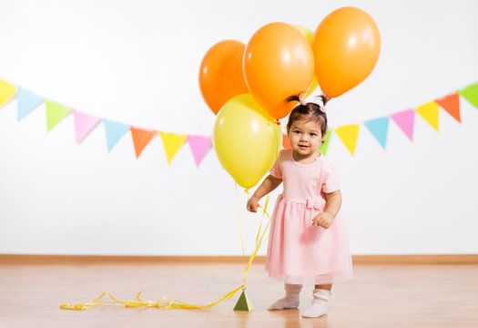 childhood, people and celebration concept - happy baby girl with helium balloons on birthday party