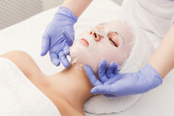 Fototapeta na wymiar Woman gets face mask by beautician at spa