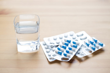 Medical capsules and glass of water on wooden table