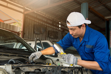 Asian mechanic in blue uniform and white hat at the repair garage, holding lamp look at the camera