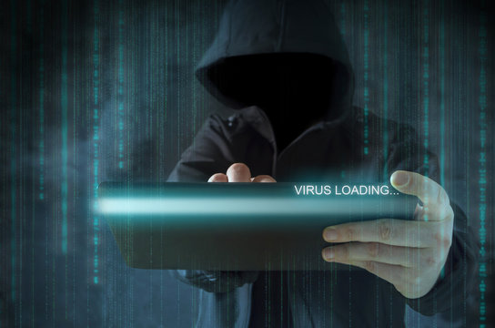 Unrecognizable hooded hacker using tablet for virus loading. Cyber crime, stealing data and identity theft concept.