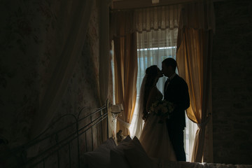 Newlyweds at wedding day. happy luxury bride and groom standing at window light in rich room, tender moment.