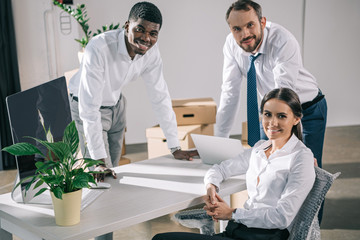 happy multiracial coworkers smiling at camera while relocating in new office