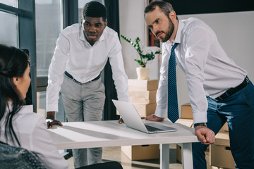 multiethnic businessmen leaning at table and looking at businesswoman in new office