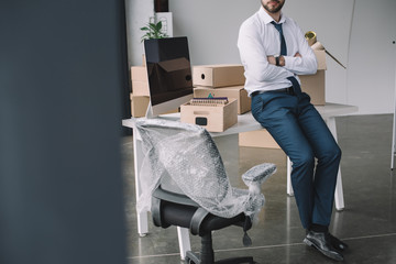 cropped shot of businessman with crossed arms sitting on table in new office during relocation