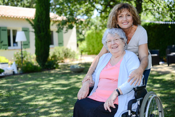 cheerful mature woman visiting her mother elderly senior female on wheel chair in retirement house hospital garden