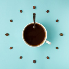 Coffee cup and roasted beans arranged as clock face on blue background, top view. Coffee time symbol. Interesting idea energy and refreshment concept.