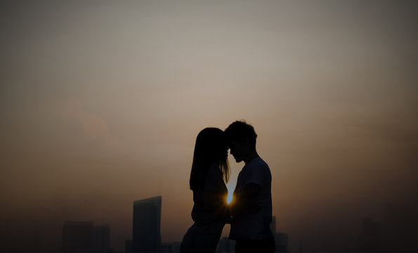 a silhouette of a couple embracing, with the sun setting behind them. The cityscape is in the background.