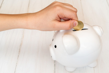 Child's hand putting a coin into piggy bank