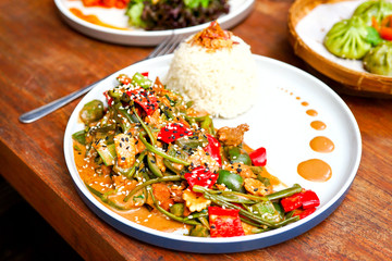 Chicken kung pao on a white plate and on a light wooden table. Chinese food. Food sticks. On the back of a blurry background, a white brick pad is covered with an word love. Side view with copy space