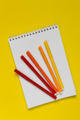 Multicolored markers on a white notepad on a yellow background flat lay top view with copy space,layout,mocap