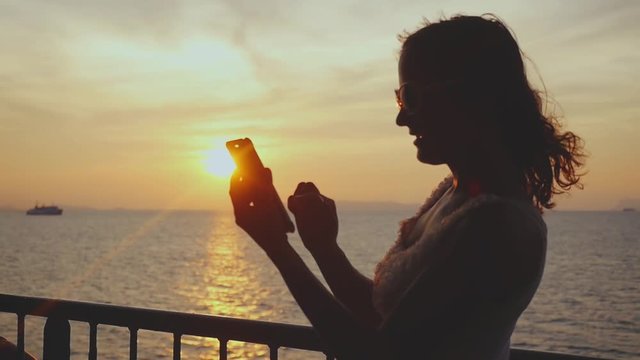 Silhouette of girl uses mobile phone while traveling on cruise ship at amazing sunset. slow motion. 1920x1080