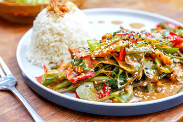 Chicken kung pao on a white plate and on a light wooden table. Chinese food. Food sticks. On the back of a blurry background, a white brick pad is covered with an word love. Top view with copy space