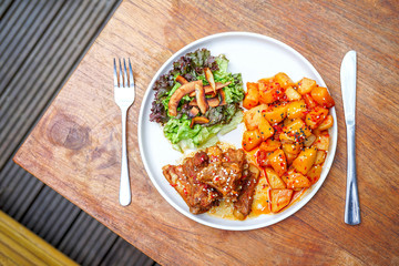 Fried pork ribs with potatoes and salad. On a white plate with a knife and fork. Wooden background - a table. Top view with copy space
