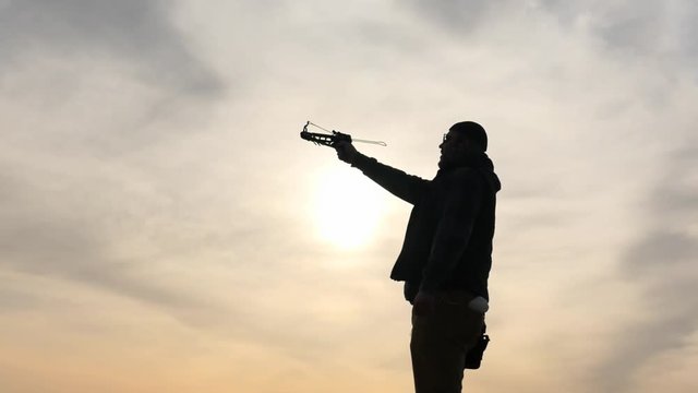 mans silhouette shoots an arrow from small crossbow dolly shot