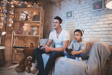 Father and son are playing video games on tv at night at home.