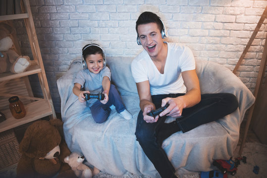 Father And Son Are Playing Video Games On Tv At Night At Home.