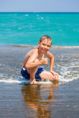 Smiling boy on beach with thumbs up