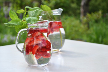 Strawberry  mint flavored water in glass jugs on summer outdoor background. Cold refreshing ...