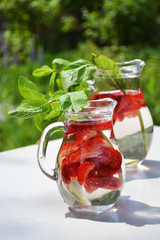 Strawberry  mint flavored water in glass jugs on summer outdoor background. Cold refreshing drinks...