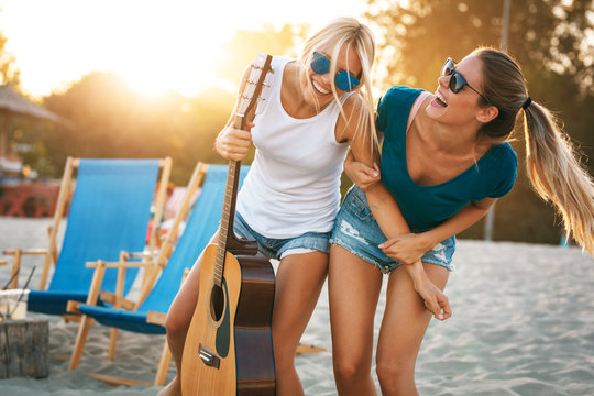 Two young female friends hangout at the beach ,singing and relaxing in beautiful summer sunset.They hug each other.